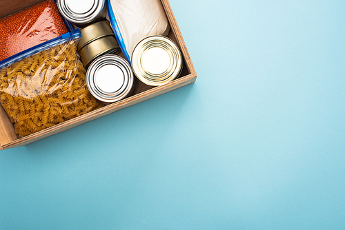 top view of cans and groats in zipper bags in wooden box on blue background