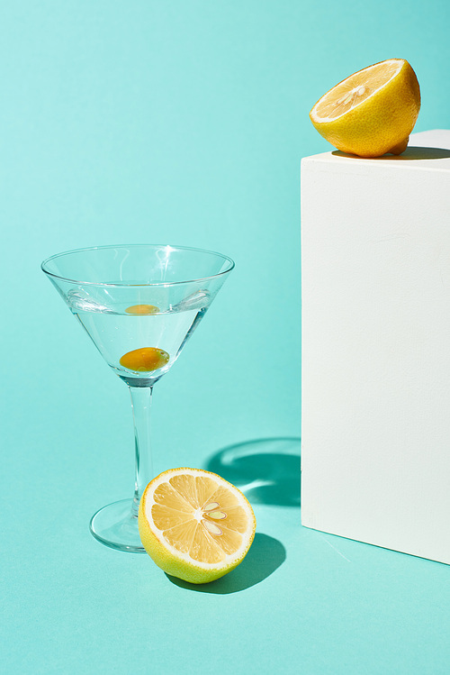 transparent glass with cocktail and olive near lemon on turquoise background
