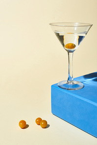 transparent glass with cocktail on blue cube on beige background