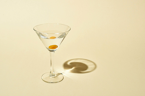 transparent glass with cocktail and olive on beige background