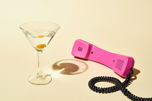 transparent glass with cocktail and olive near pink vintage phone on beige background