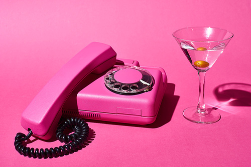 cocktail with olive and retro bright pink telephone on pink background