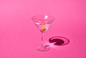 transparent glass with cocktail and olive on pink background