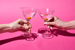 cropped view of women holding glasses with cocktails on pink background
