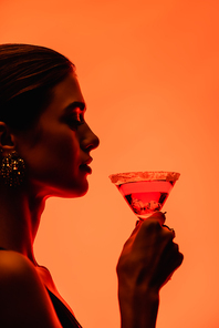 side view of young woman holding margarita cocktail on orange