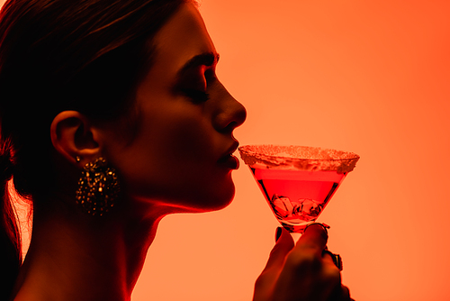 side view of young woman with closed eyes drinking margarita cocktail on orange