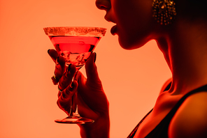 cropped view of woman drinking margarita cocktail on orange