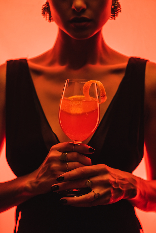 cropped view of elegant woman holding glass with mixed cocktail and orange on pink