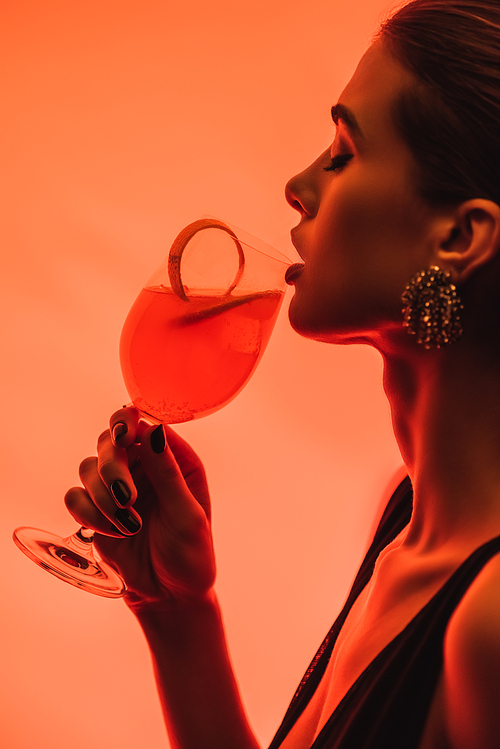 profile of woman holding glass with mixed cocktail and orange peel on pink