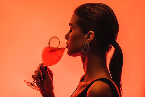 side view of woman drinking mixed cocktail and orange on pink