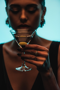 glass of martini with olive in hand of woman on blurred background isolated on blue