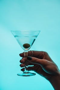 cropped view of woman holding glass of martini with olive isolated on blue