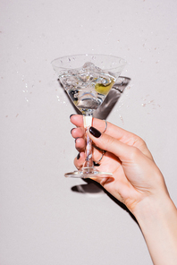 cropped view of woman shaking glass of martini with olive near drops of alcohol on white