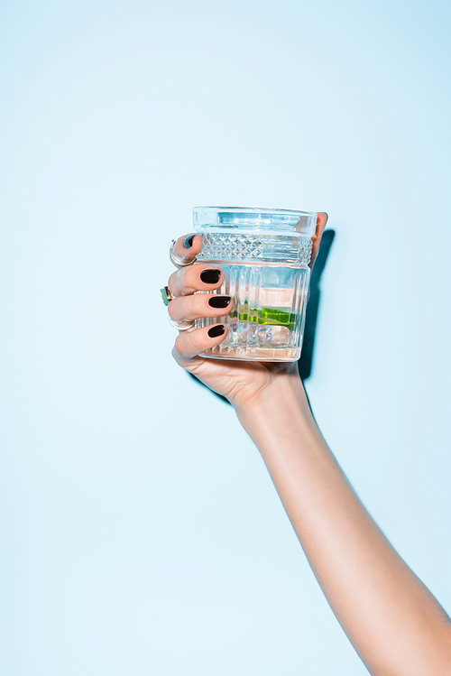 cropped view of woman holding glass with lime in alcohol drink on blue