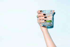 cropped view of young woman holding glass with lime in alcohol drink on blue