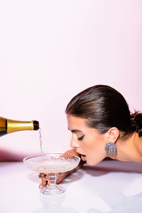 brunette woman drinking champagne from glass near bottle on white