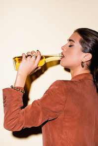 side view of brunette woman in brown blazer drinking beer on white
