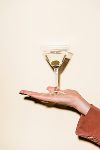 cropped view of woman holding glass of martini with green olive in hand on white