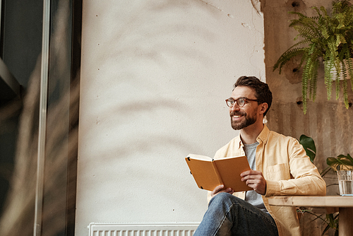 cheerful and bearded man holding notebook and looking away
