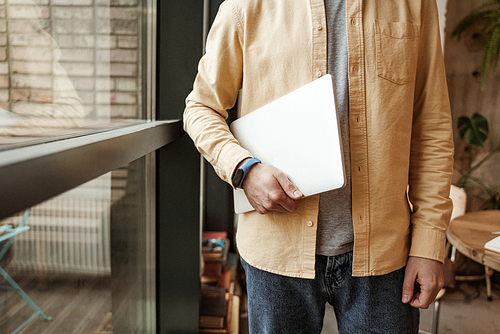 cropped view of freelancer holding laptop while standing near window