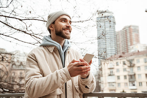happy bearded man in beanie hat holding smartphone