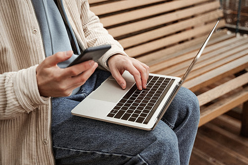 cropped view of freelancer using smartphone while typing on laptop