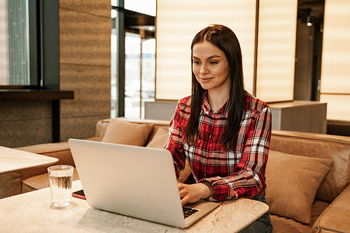 brunette freelancer using laptop while working remotely in cafe