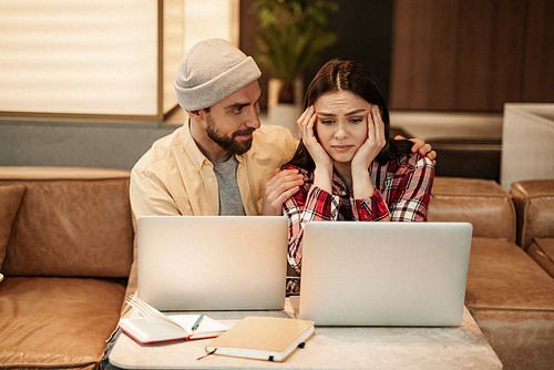bearded freelancer calming worried woman looking at laptop