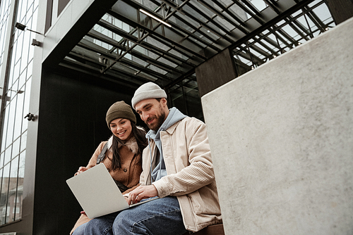 low angle view of freelancers in beanie hats smiling while using laptop