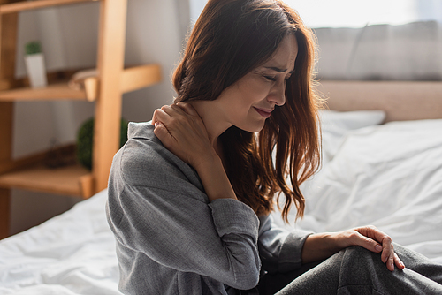 upset brunette woman suffering from neck pain in bedroom