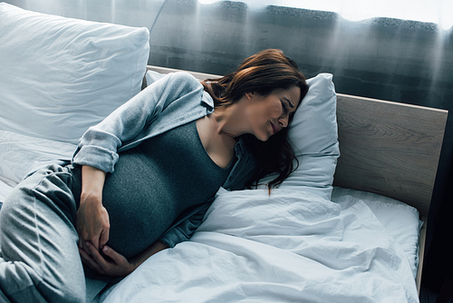 pregnant woman with closed eyes suffering from pain on bed