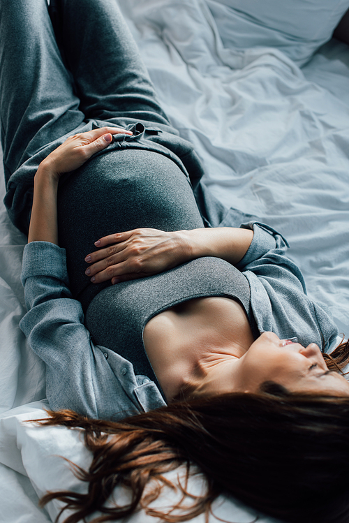 overhead view of pregnant woman suffering from pain on bed
