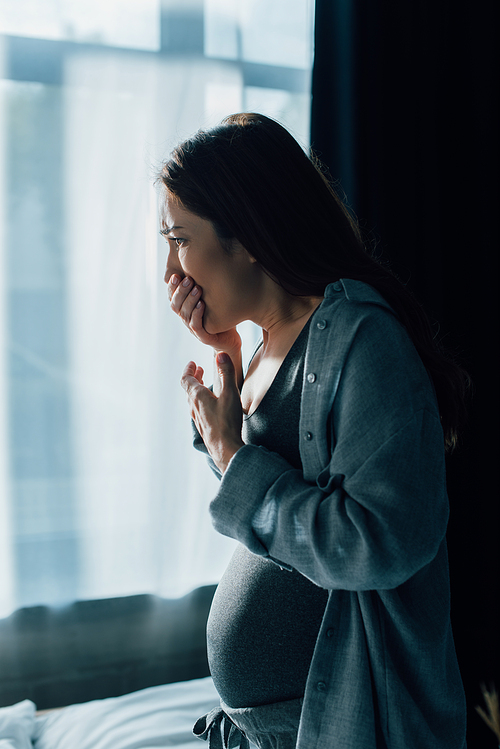 brunette pregnant woman covering mouth while having nausea at home