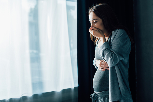 brunette pregnant woman covering mouth while having nausea while standing at home