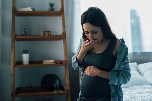 pregnant woman touching belly and covering mouth while having nausea at home