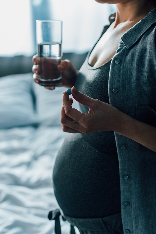 cropped view of pregnant woman holding glass of water and pill