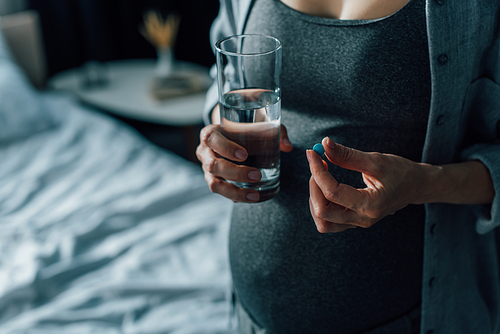 partial view of pregnant woman holding glass of water and pill