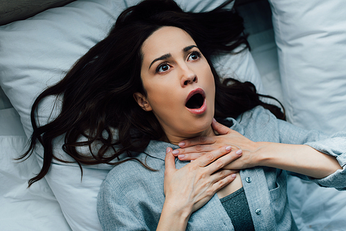 top view of scared brunette woman touching throat while lying on bed