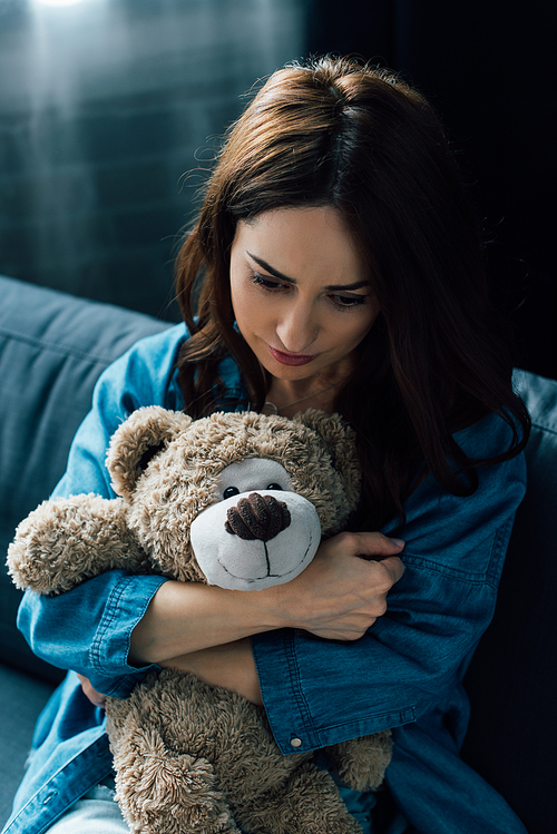 depressed brunette woman holding teddy bear and looking down