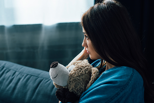 depressed brunette woman holding teddy bear while looking away