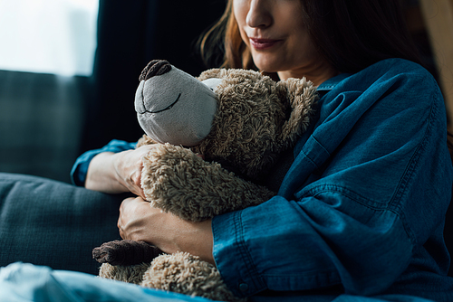 cropped view of depressed brunette woman holding teddy bear