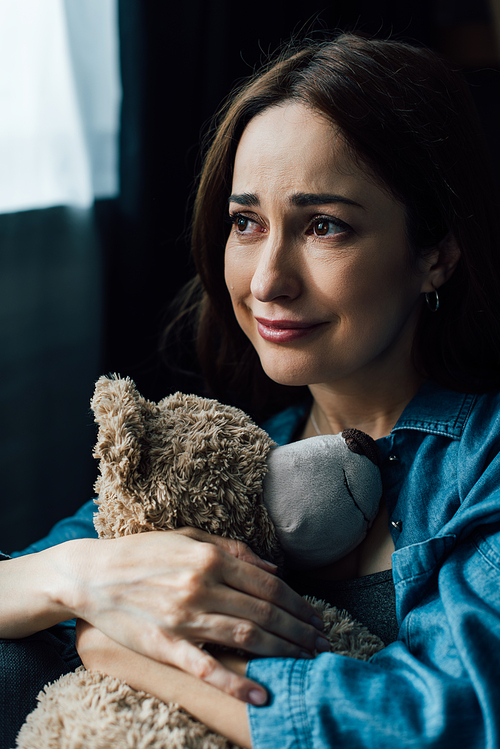 upset brunette woman holding teddy bear and looking away