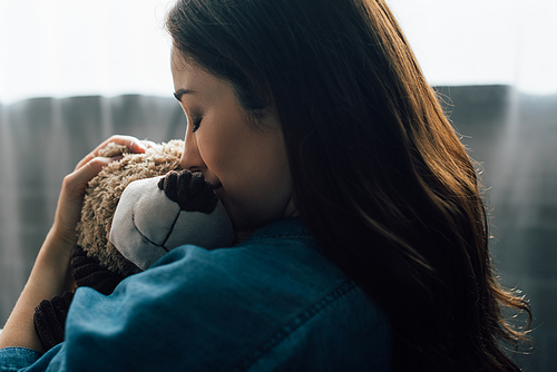 upset brunette woman with closed eyes hugging teddy bear