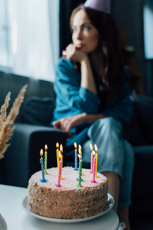 selective focus of birthday cake on coffee table near sad woman