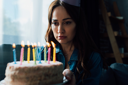 selective focus of sad woman looking at birthday cake with candles