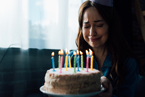 selective focus of sad woman crying while holding birthday cake with candles