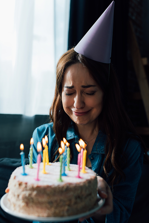 selective focus of upset woman crying while holding birthday cake with candles