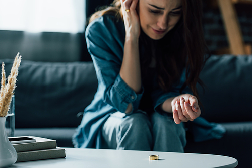 selective focus of golden ring on coffee table near upset woman, divorce concept