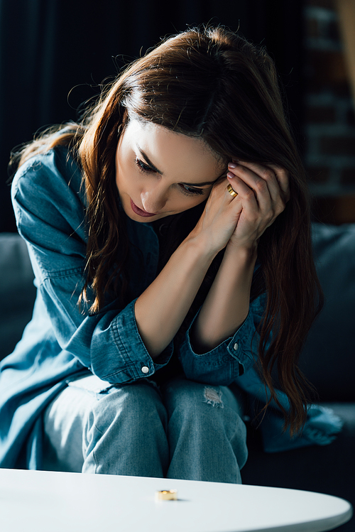 depressed woman sitting near coffee table with golden ring, divorce concept