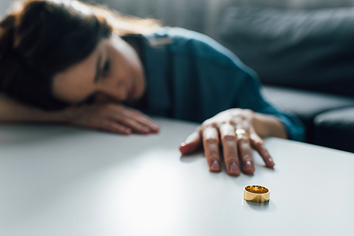 selective focus of upset woman reaching golden ring on coffee table, divorce concept